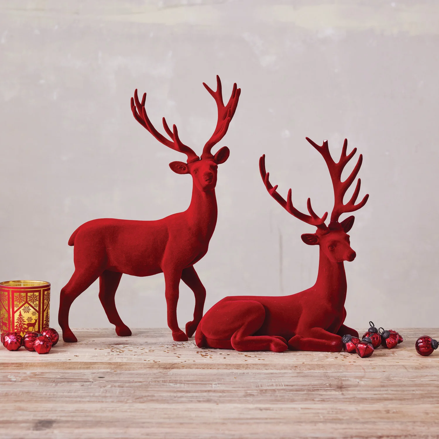 Two red deer figurines on a wooden surface with a light gray background
