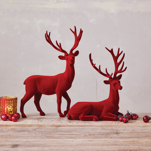 Two red deer figurines on a wooden surface with a light gray background