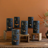 Set of blue jack-o'-lantern candle holders on a wooden table against an orange wall.
