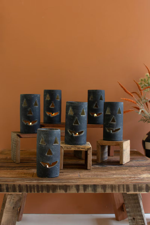 Set of blue jack-o'-lantern candle holders on a wooden table against an orange wall.