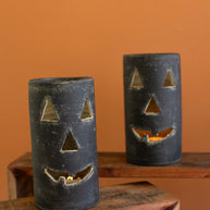 Two black jack-o'-lantern candle holders on a wooden surface against an orange wall.