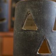 Black ceramic vase with triangular cutouts on a blurred background