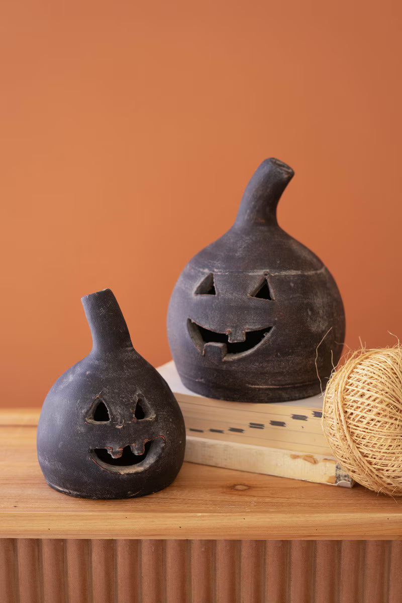 Two black ceramic jack-o'-lanterns on a wooden surface with an orange background