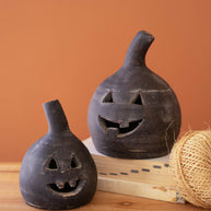 Two black ceramic jack-o'-lanterns on a wooden surface with an orange background