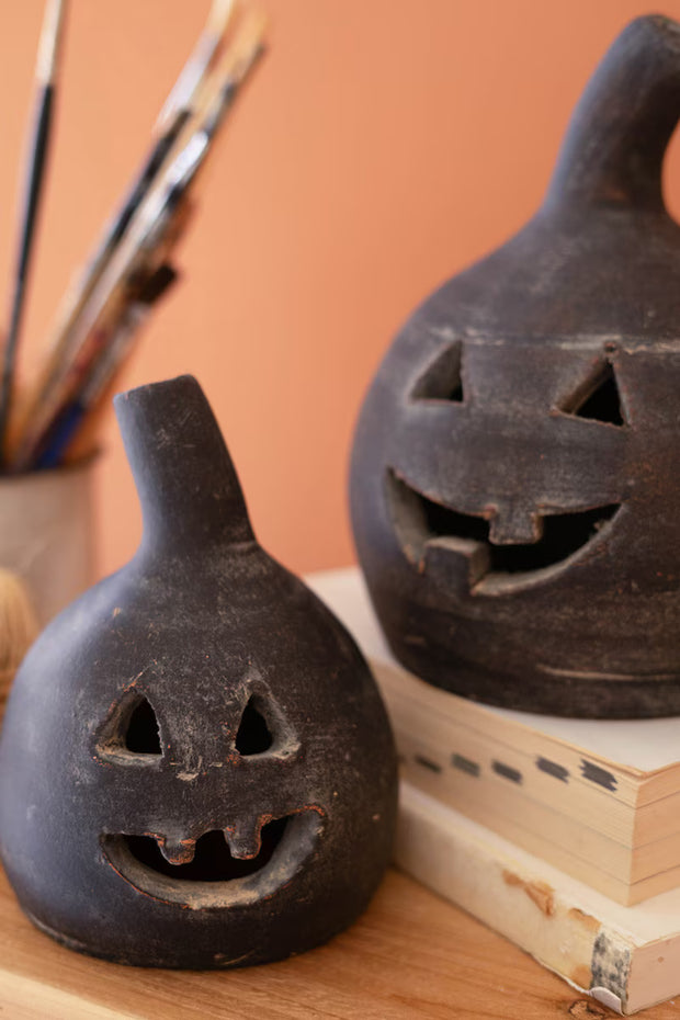 Two black ceramic jack-o'-lanterns on a wooden surface with paintbrushes in the background.