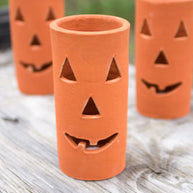 Three terracotta pots with jack-o'-lantern faces on a wooden surface.