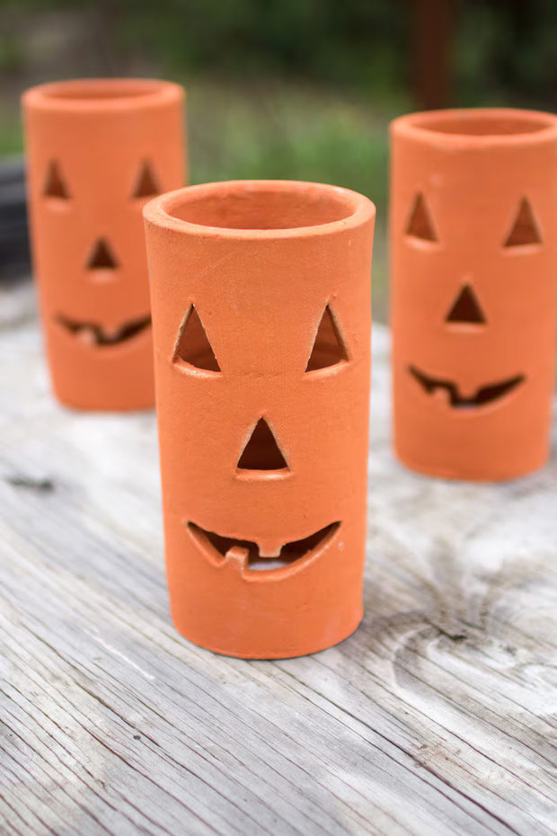 Three terracotta pots with jack-o'-lantern faces on a wooden surface.