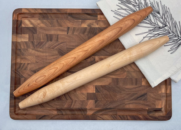 Two wooden rolling pins on a wooden cutting board with a white towel in the background.