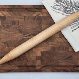 Wooden cutting board with a rolling pin and a towel on a light background