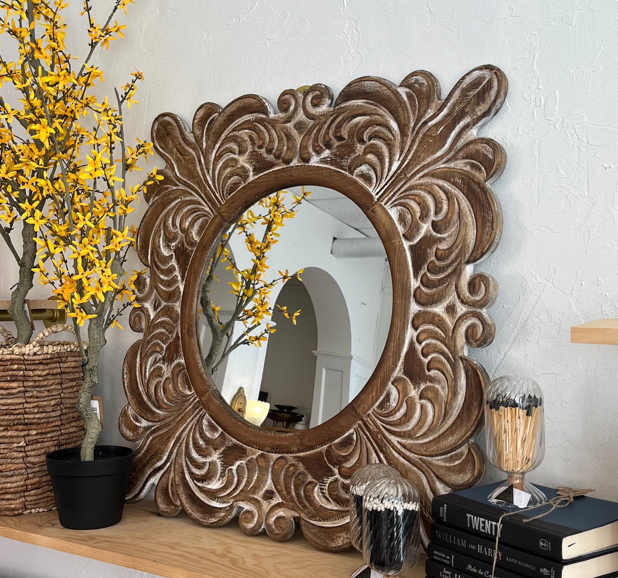 Decorative wall mirror with intricate carvings on a shelf with books and decorative items.