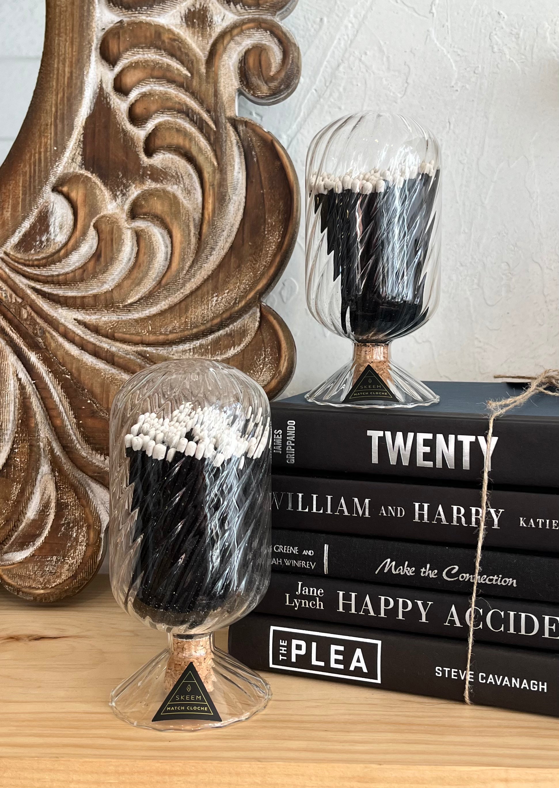 Decorative glass containers with black and white contents on a stack of books against a wooden wall.