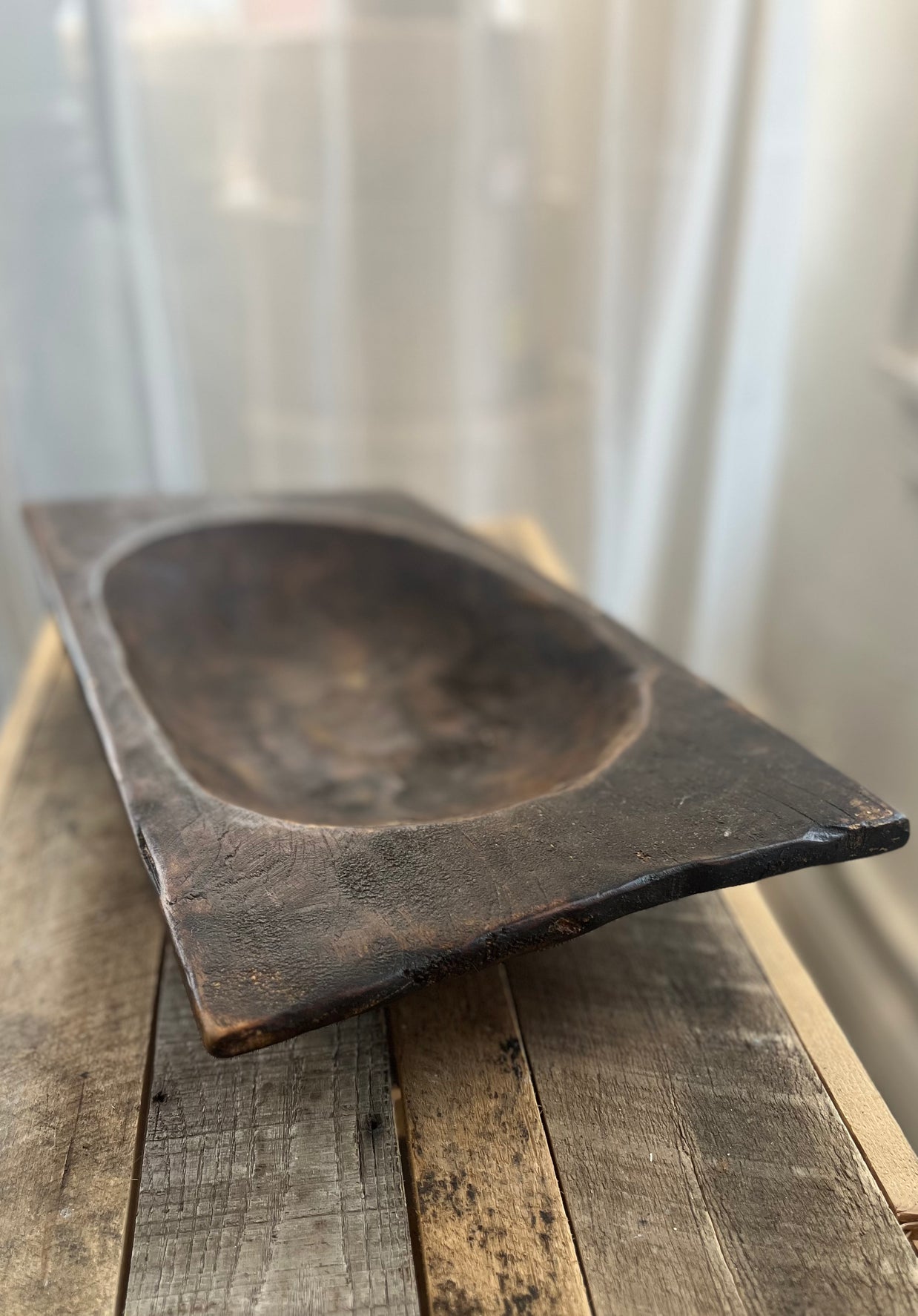 Rectangular wooden bowl on a wooden surface with a white curtain background
