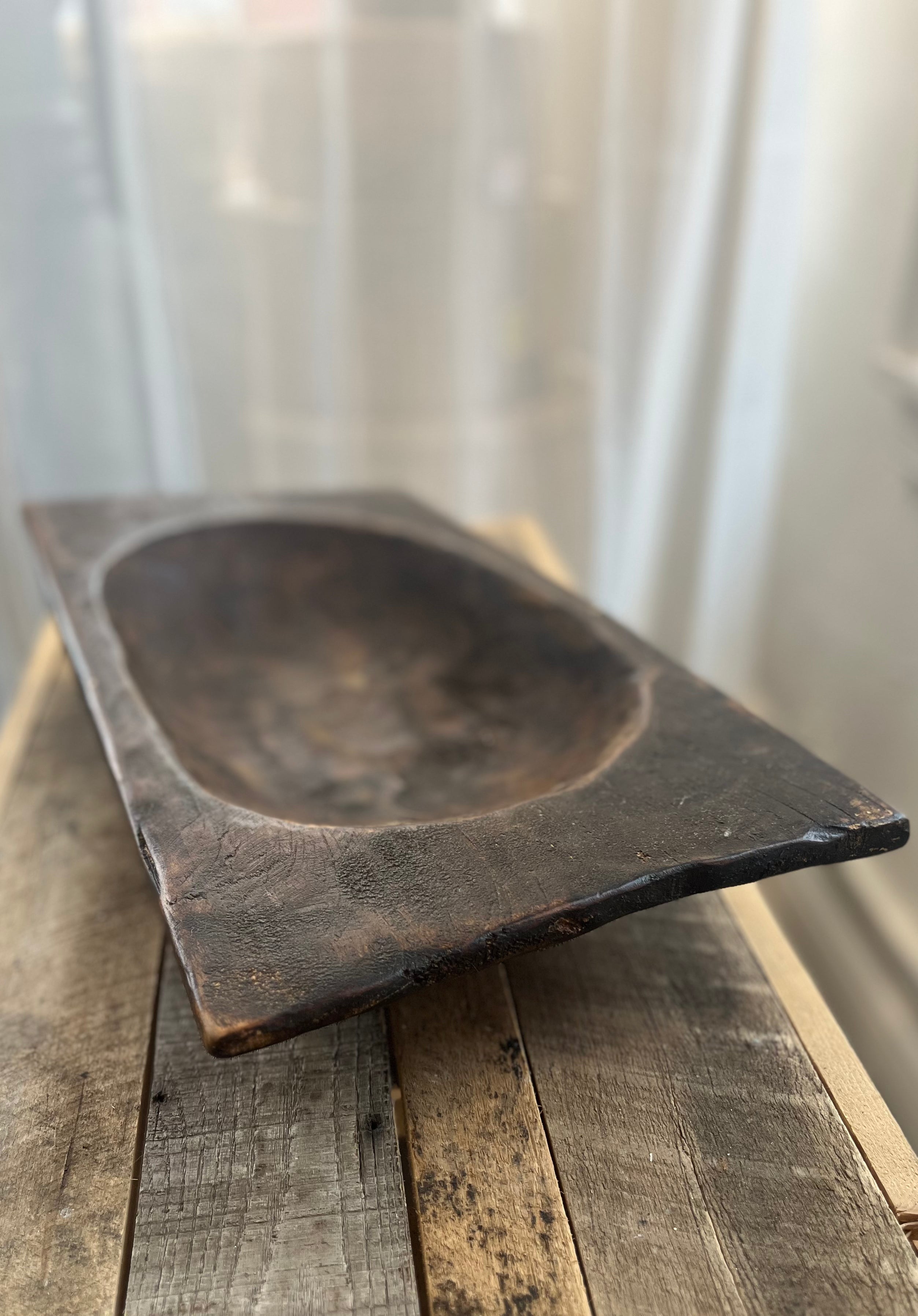 Rectangular wooden bowl on a wooden surface with a white curtain background