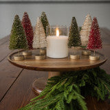Decorative setup with small Christmas trees and a candle on a wooden surface.