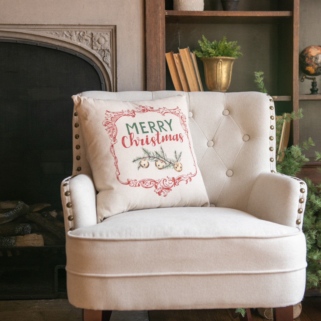 Beige armchair with a 'Merry Christmas' pillow in a cozy room with a fireplace and bookshelf.