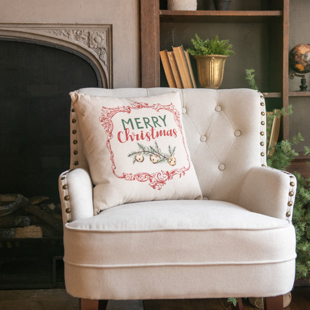 Beige armchair with a 'Merry Christmas' pillow in a cozy room with a fireplace and bookshelf.