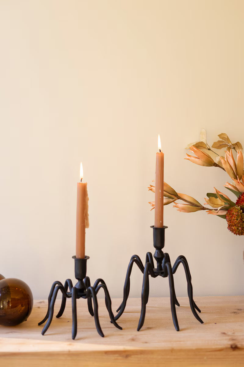 Two candle holders with lit candles on a wooden surface against a beige wall.
