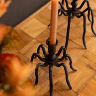 Spider-like candle holder with a lit candle on a wooden surface