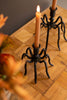 Spider-like candle holder with a lit candle on a wooden surface