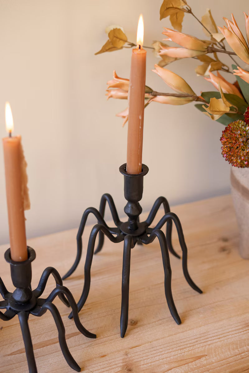 Black spider-like candle holder with two lit candles on a wooden surface.