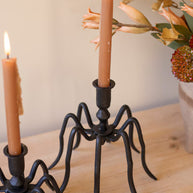Black spider-like candle holder with two lit candles on a wooden surface.