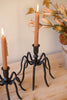 Black spider-like candle holder with two lit candles on a wooden surface.