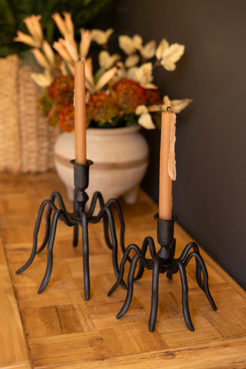Decorative candle holders with candles on a wooden surface with a floral arrangement in the background.
