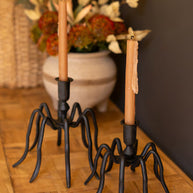 Decorative candle holders with candles on a wooden surface with a floral arrangement in the background.