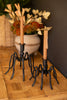 Decorative candle holders with candles on a wooden surface with a floral arrangement in the background.