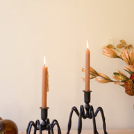 Two candle holders with lit candles on a wooden surface against a beige wall.