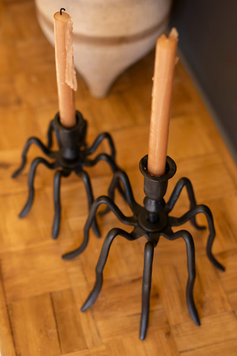 Spider-shaped candle holders with candles on a wooden floor.