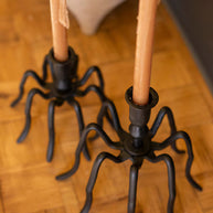 Spider-shaped candle holders with candles on a wooden floor.