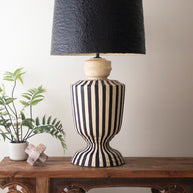 Black and white striped lamp on a wooden console table with a plant and books in the background.