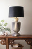 Black and white striped lamp on a wooden console table with a plant and books in the background.