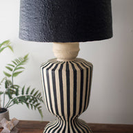Decorative lamp with black and white striped base and black textured shade on a wooden surface.