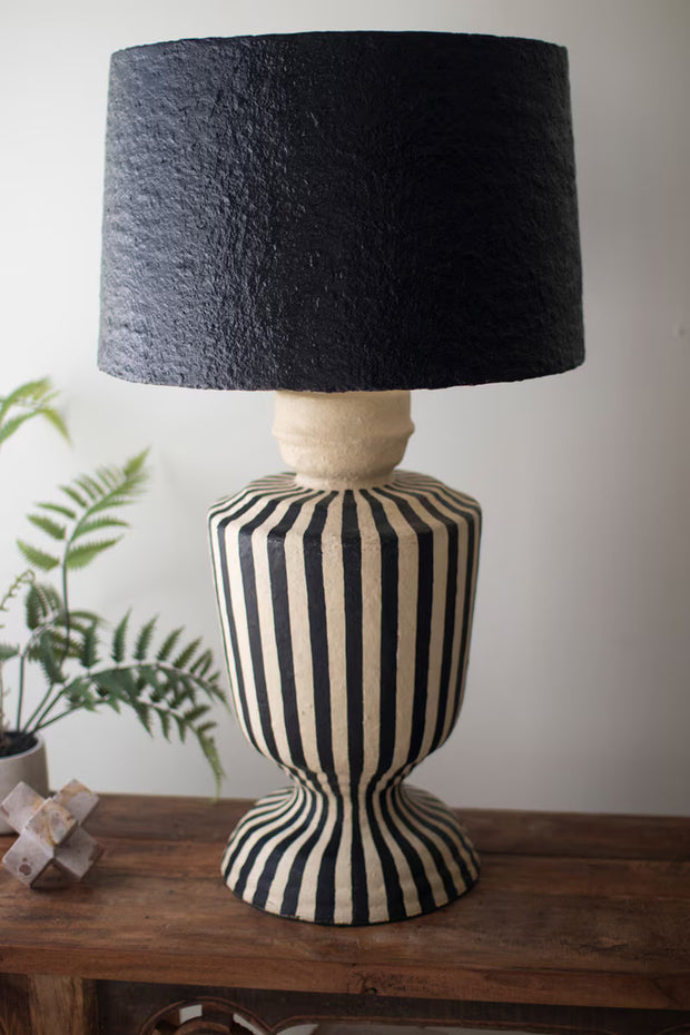 Decorative lamp with black and white striped base and black textured shade on a wooden surface.