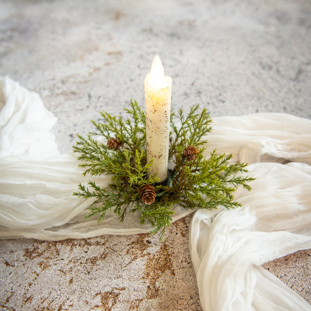 Candle in a decorative holder with greenery on a textured surface with white fabric.
