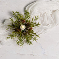 Decorative arrangement with greenery and a candle on a textured white surface