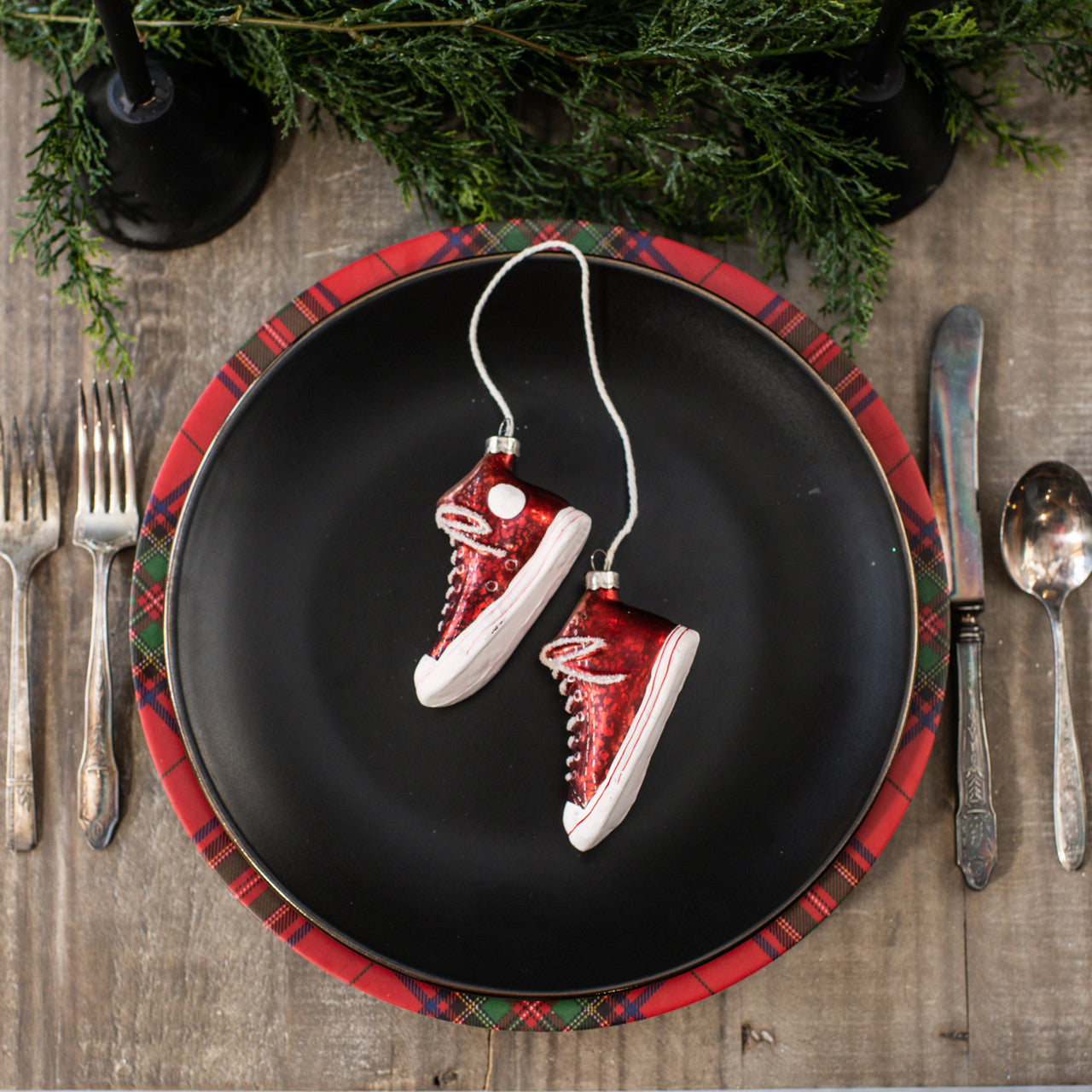 Red and white sneaker ornaments on a black plate with plaid rim, surrounded by Christmas decorations.