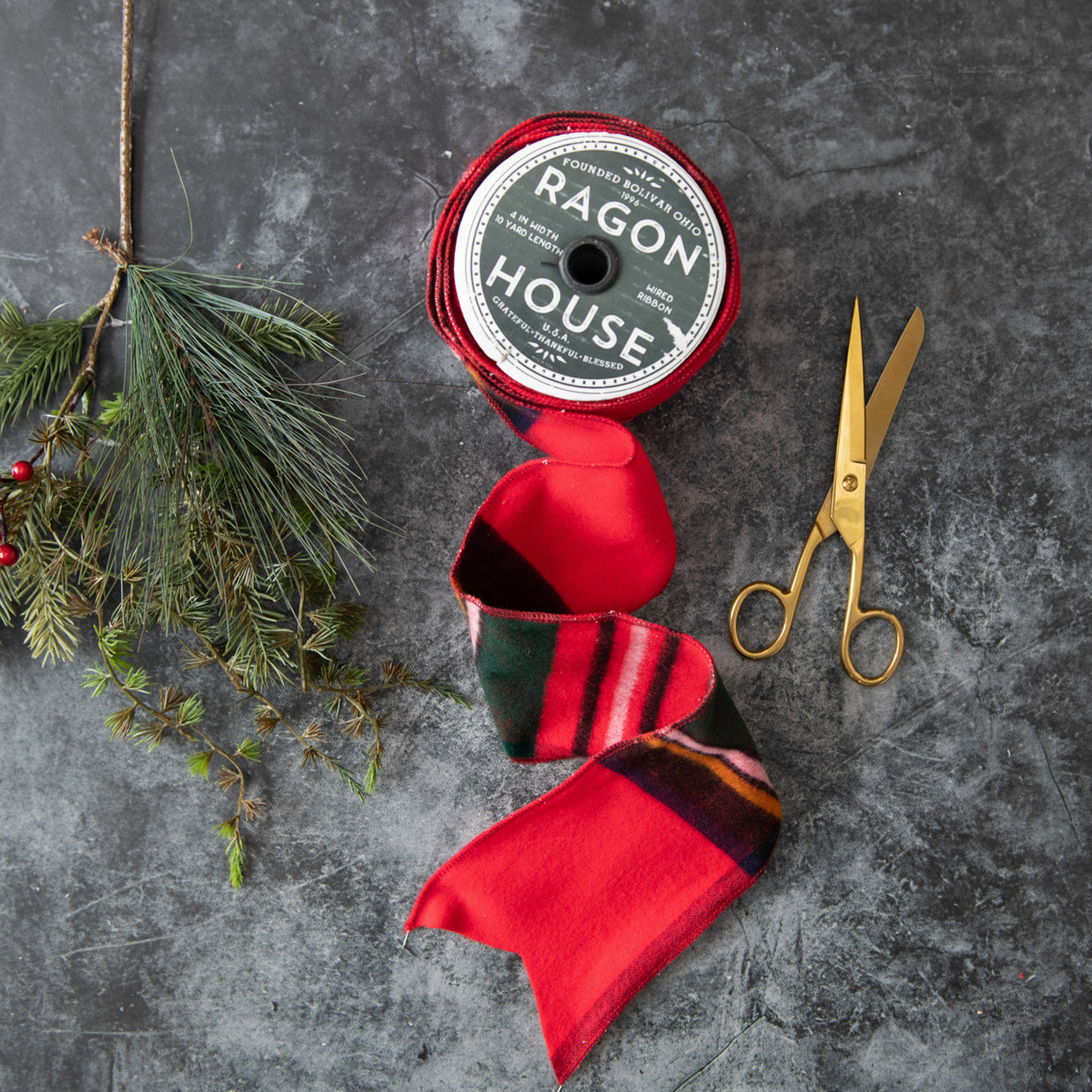 Red ribbon with a 'Ragon House' label, scissors, and greenery on a gray surface