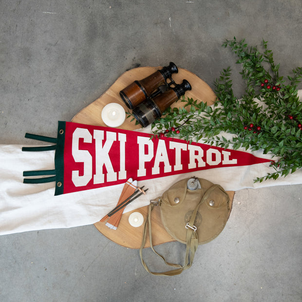 Ski patrol banner with binoculars, pouch, and greenery on a gray surface
