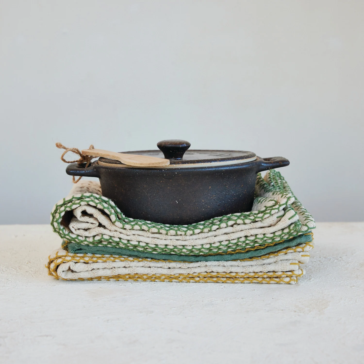 Black pot with a lid on top of folded green and white patterned cloths on a light surface.