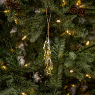 Decorative fish ornament hanging on a Christmas tree with lights and pinecones.