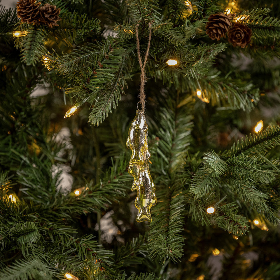 Decorative fish ornament hanging on a Christmas tree with lights and pinecones.