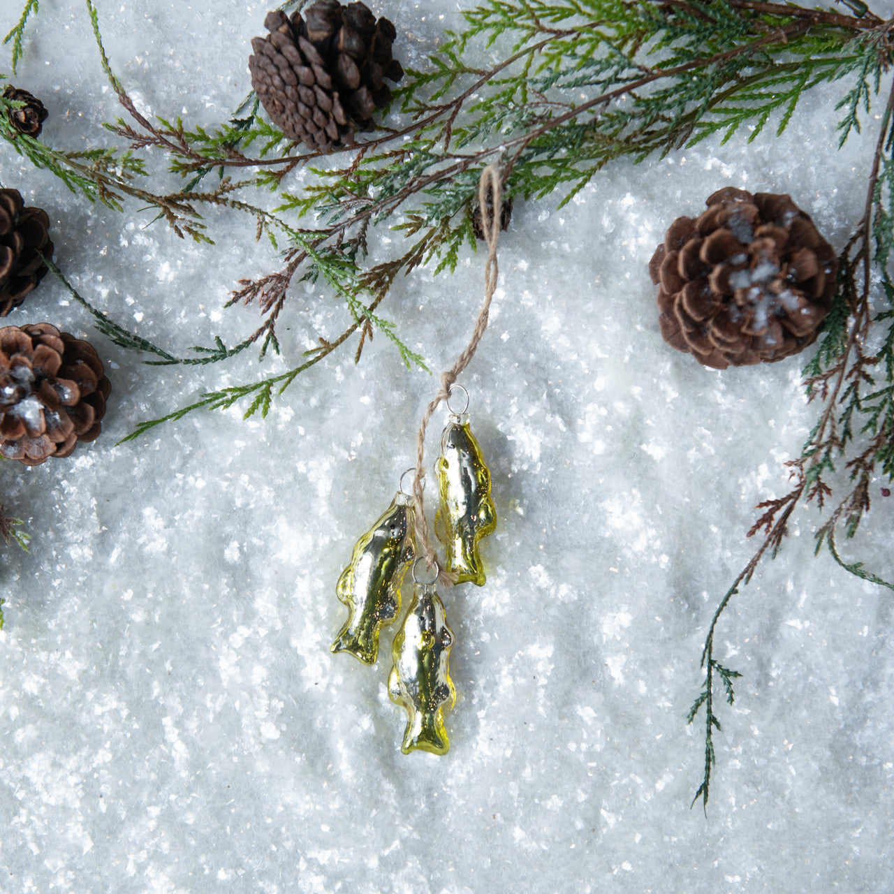 Decorative gold fish ornaments on a snowy background with pine branches and cones.
