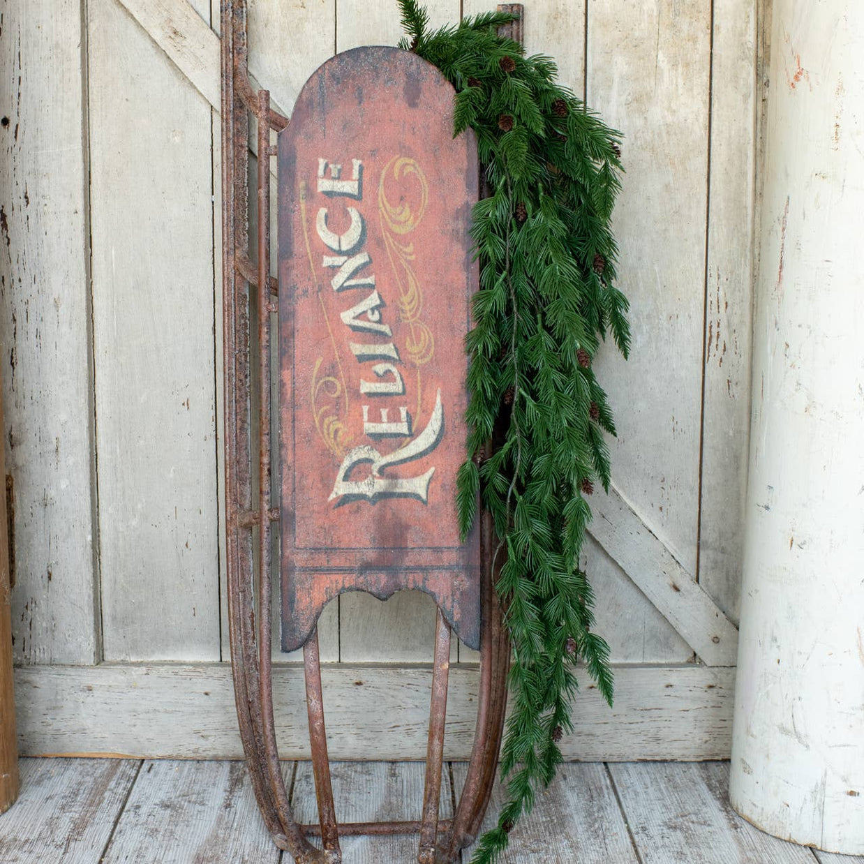 Vintage sled with 'Reliance' branding and greenery against a wooden wall.
