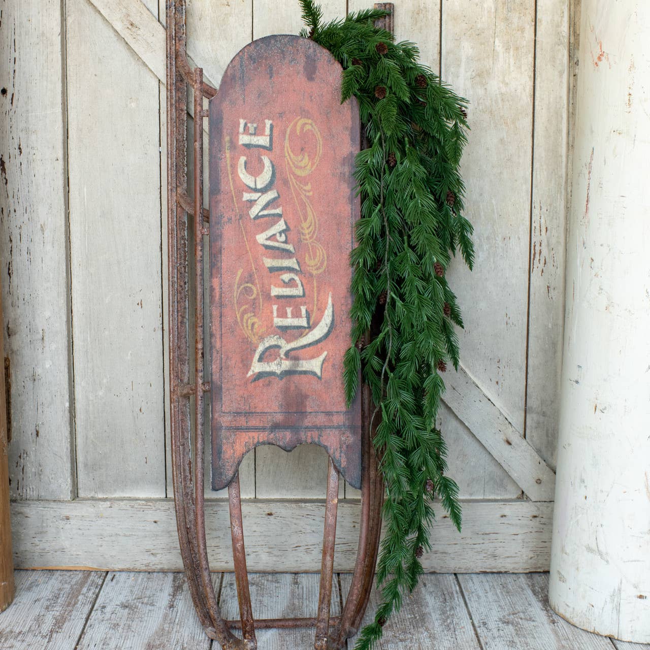 Vintage sled with 'Reliance' branding and greenery against a wooden wall.