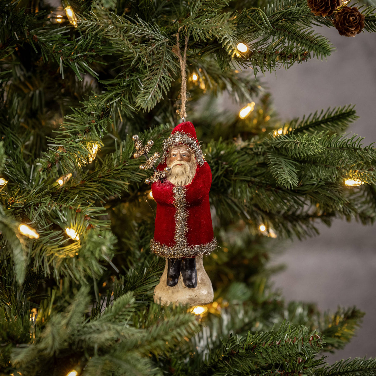 Decorative Santa Claus ornament hanging on a Christmas tree with lights.