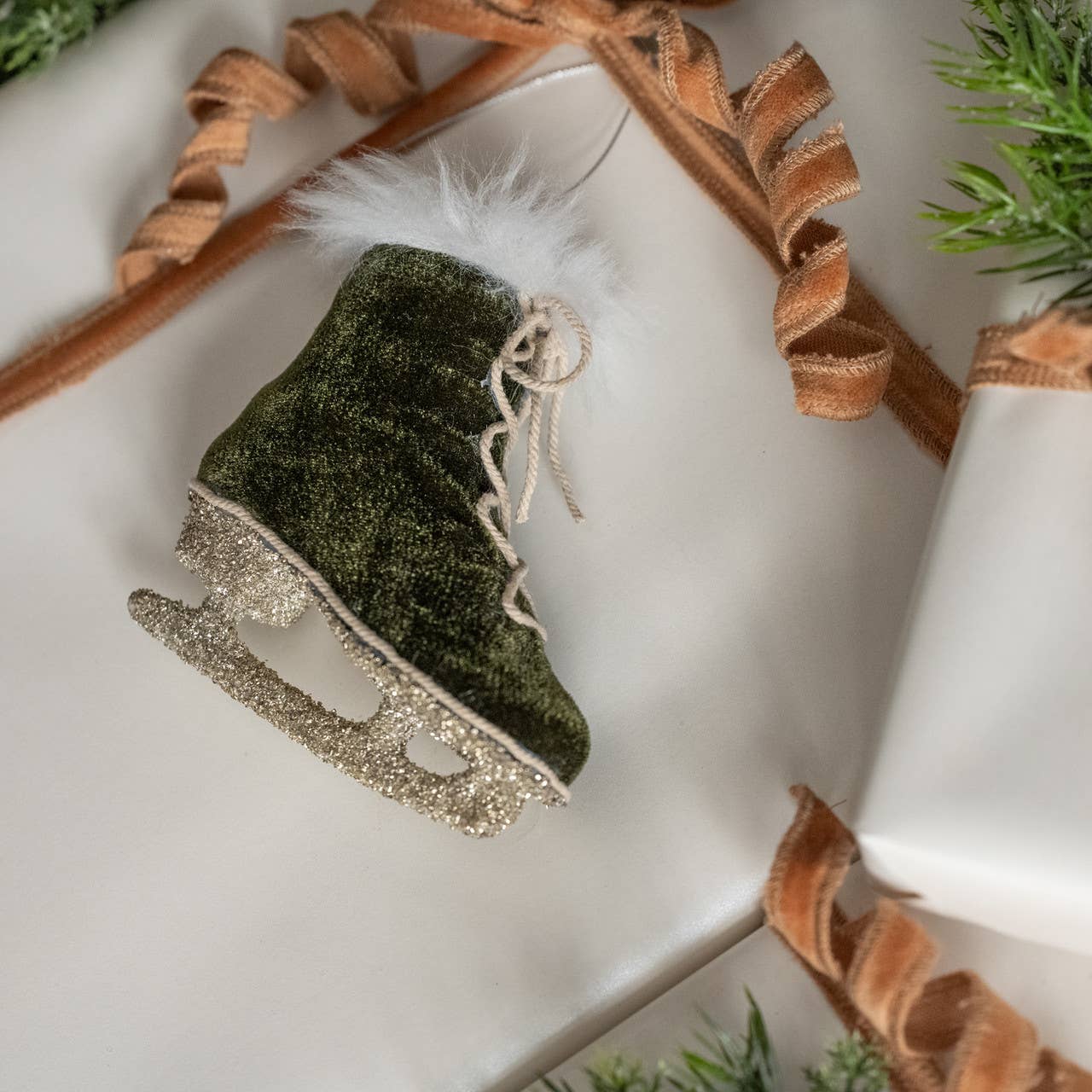Green textured ice skate ornament with gold glittery base on a white surface with decorative elements.
