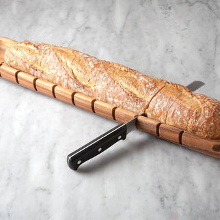 Wooden bread knife with a loaf of bread on a marble surface